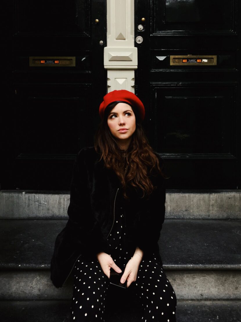 Betty Autier en béret rouge assise devant une porte noire à Amsterdam