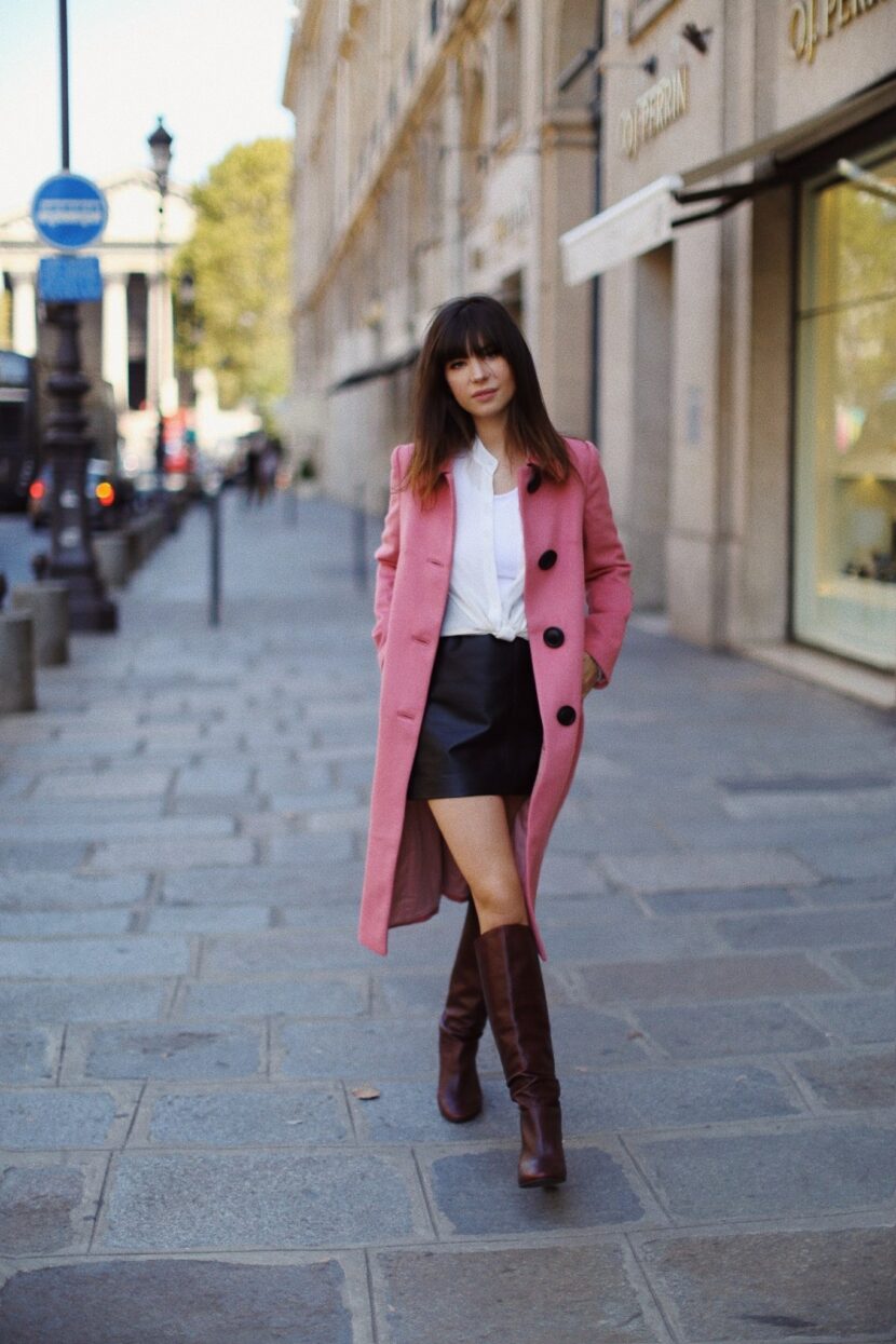 Betty Autier en manteau rose Boden, jupe en cuir et bottes hautes dans une rue de Paris