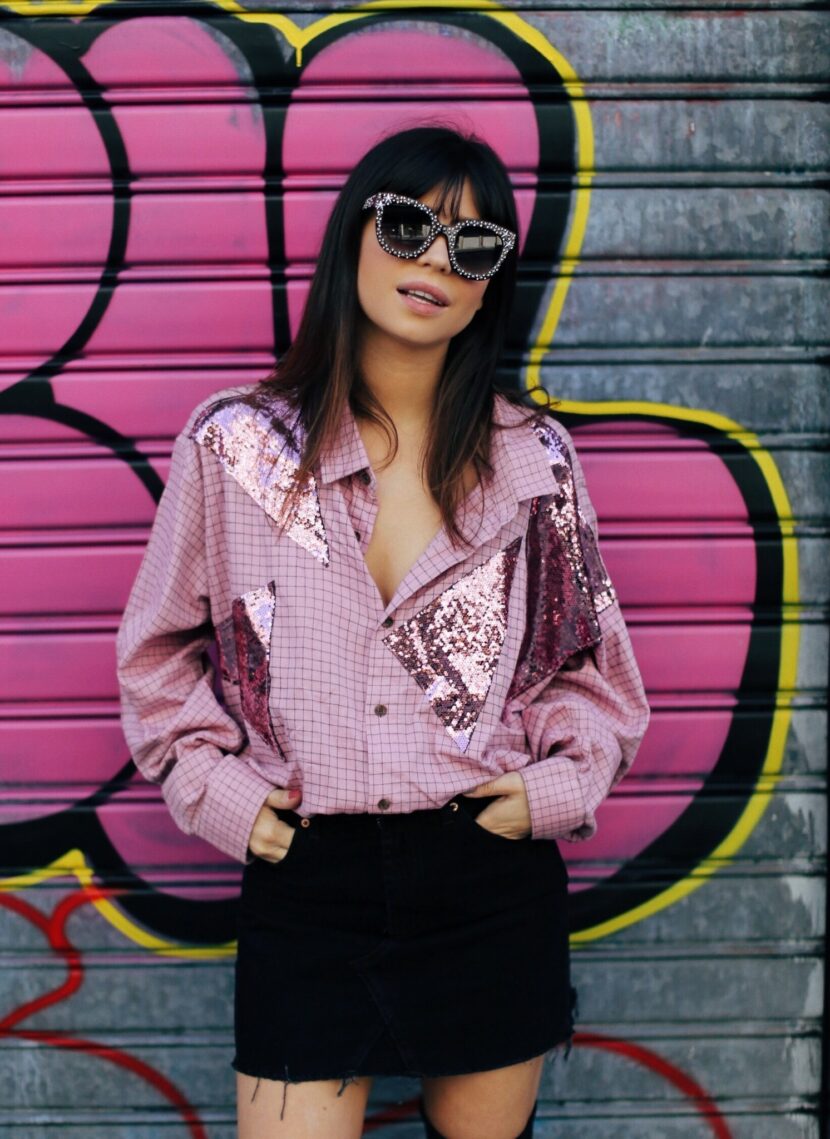 Betty Autier en chemise rose à paillettes vintage devant un graffiti