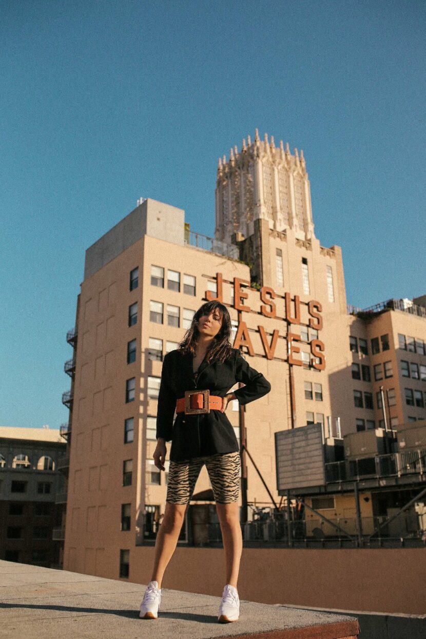 Betty Autier devant l’enseigne Jesus Saves de l’Ace Hotel à Los Angeles, blazer noir et cycliste zébré