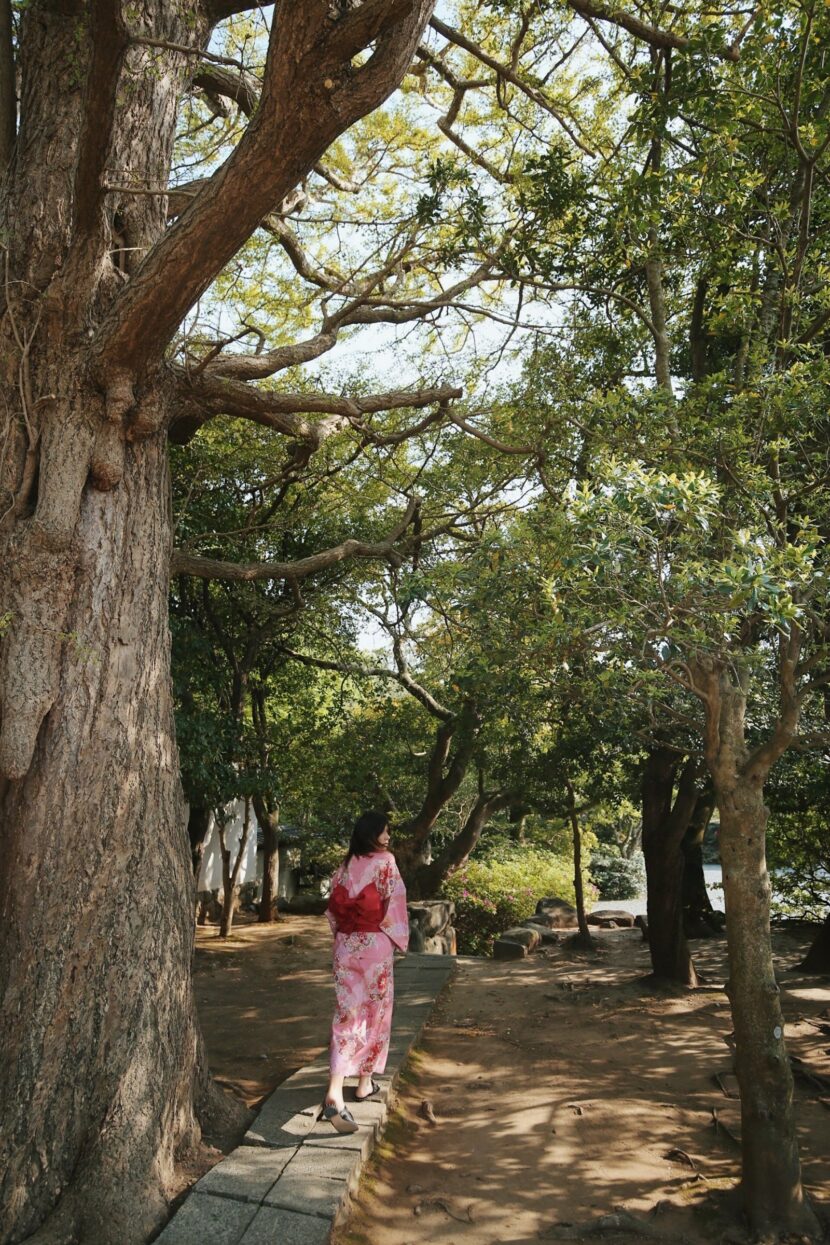Betty Autier en kimono rose dans un jardin sous les grands arbres de Kamakura