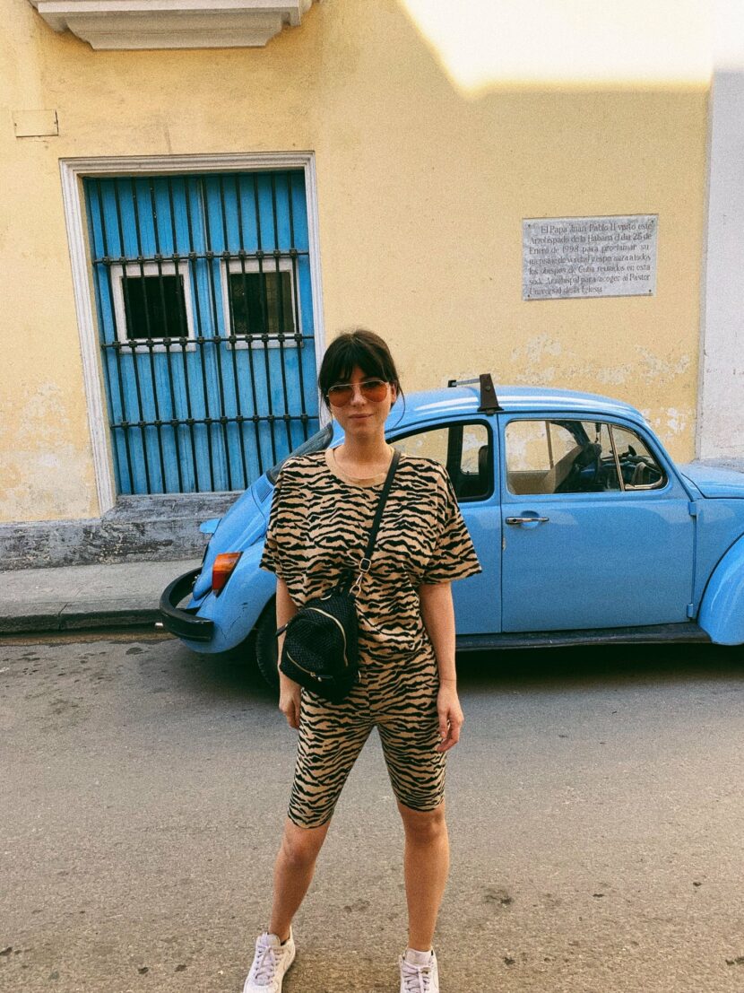 Betty Autier en t-shirt et cycliste imprimé tigre devant une Coccinelle bleue à La Havane
