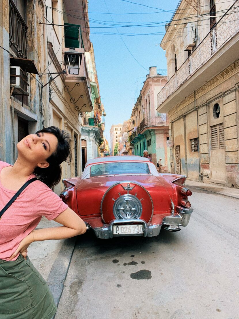 Betty Autier en t-shirt rose devant une voiture rouge à La Havane