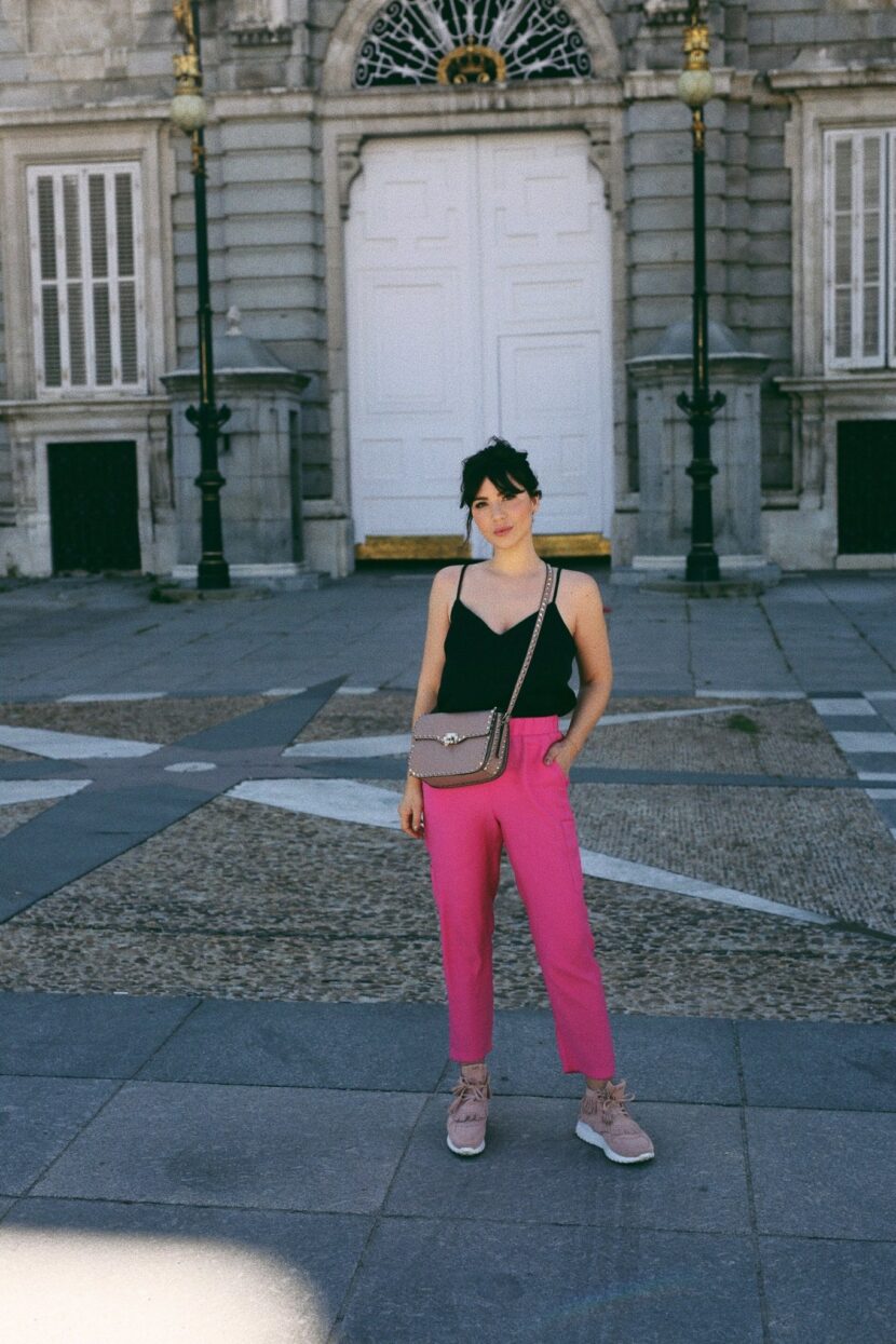 Betty Autier en top noir, pantalon rose et sac à clous devant le Palais royal de Madrid