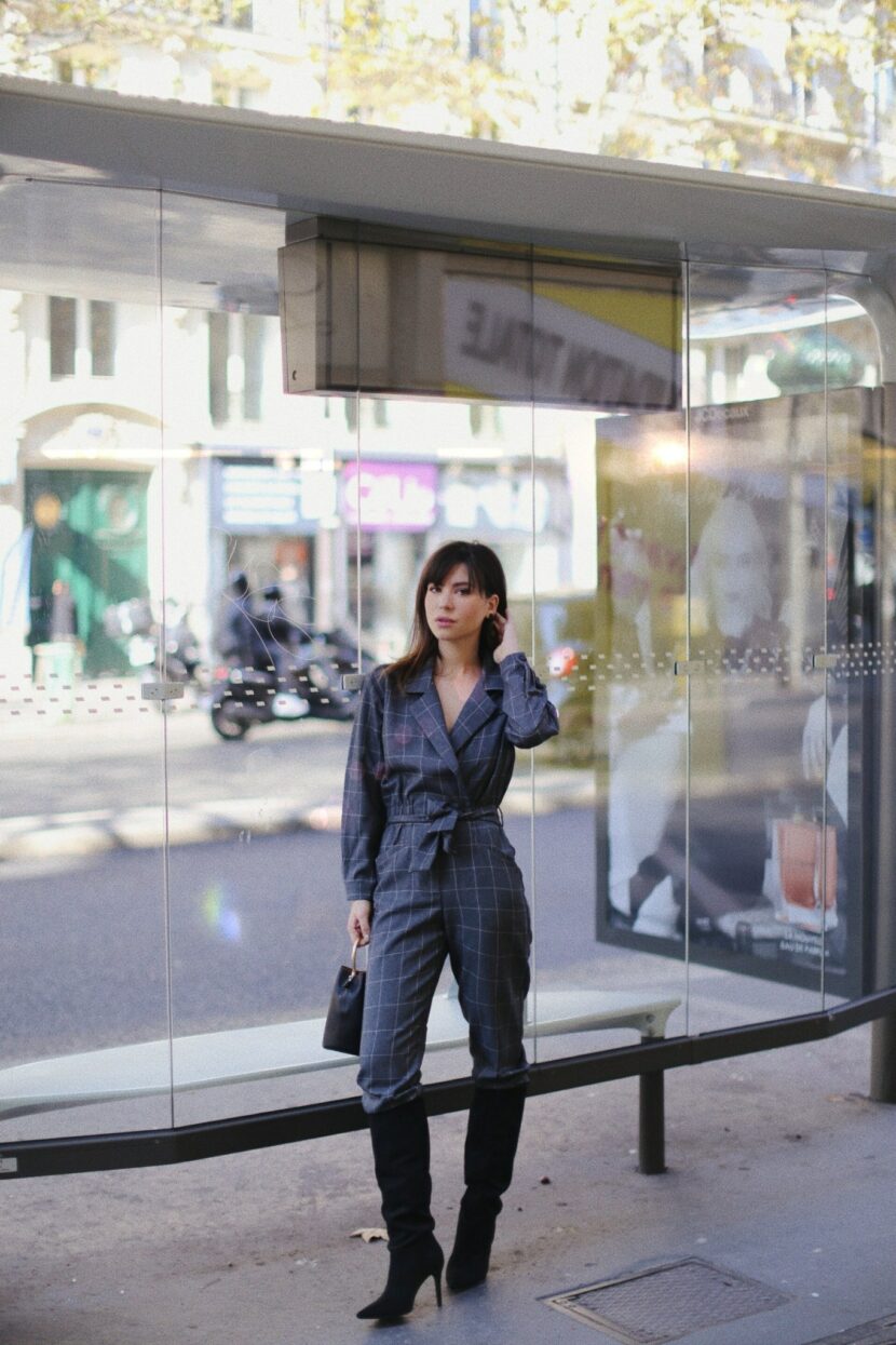 Betty Autier en combinaison à carreaux Mango et bottes noires devant un abribus