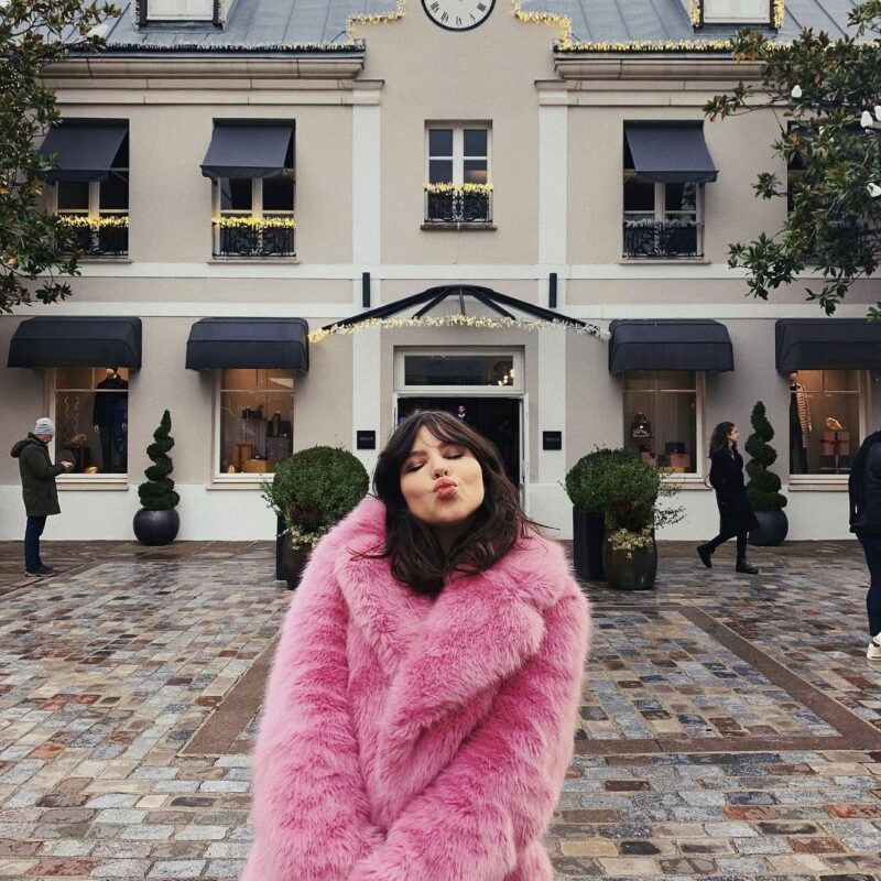 Betty Autier en manteau rose fausse fourrure devant La Vallée Village décoré pour Noël