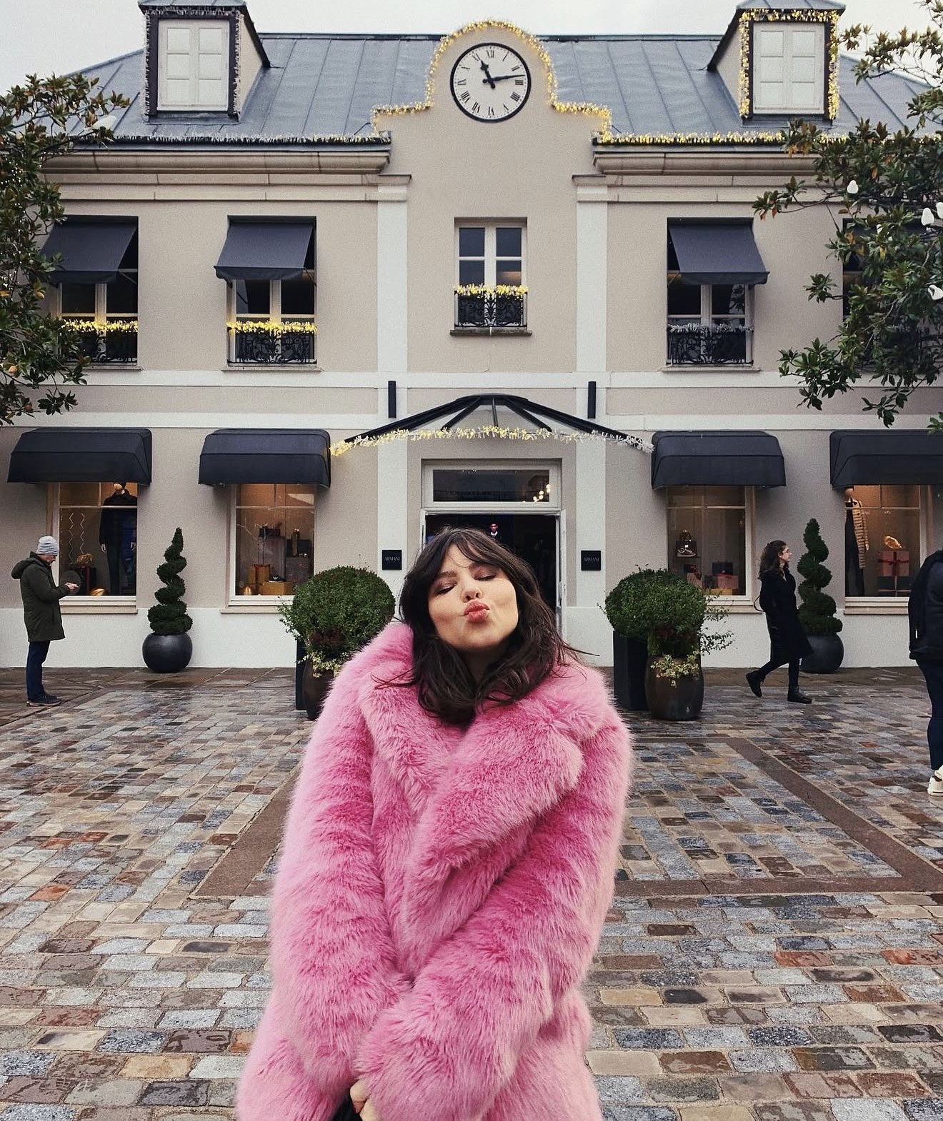 Betty Autier en manteau rose fausse fourrure devant La Vallée Village décoré pour Noël
