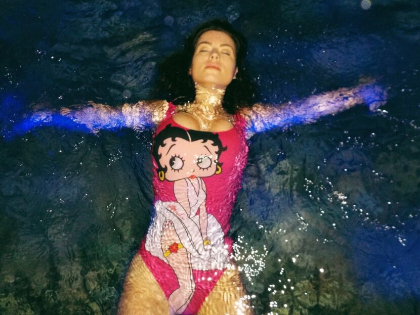 Betty Autier flotte dans la piscine de nuit en maillot Betty Boop Moschino