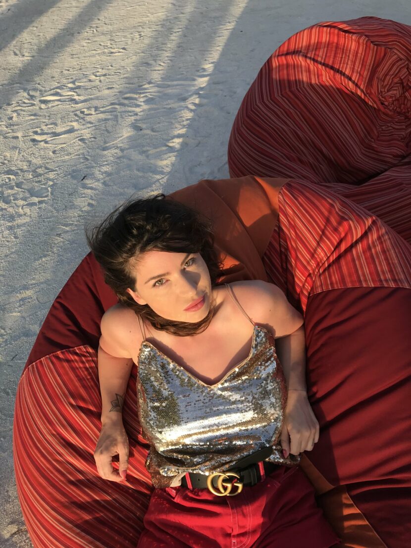 Betty Autier allongée sur un pouf rouge au Fanditha, top à sequins