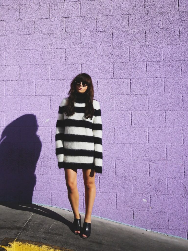 Betty Autier en pull rayé John Galliano et mules noires devant un mur violet