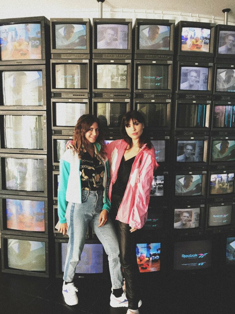Betty Autier et une amie devant le mur de télévisions Reebok