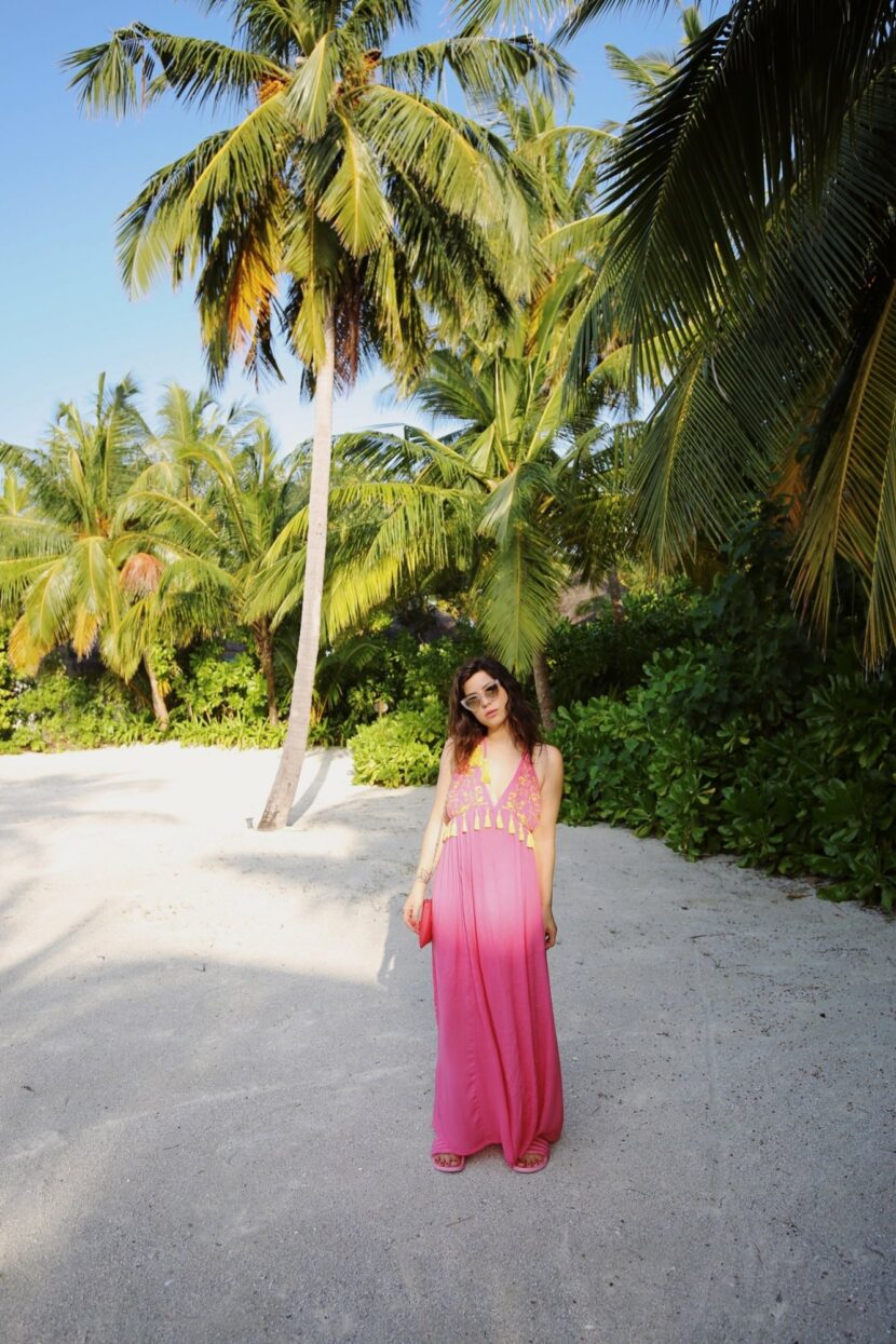 Betty Autier en robe longue rose à pompons jaunes sous les palmiers du One&Only Reethi Rah
