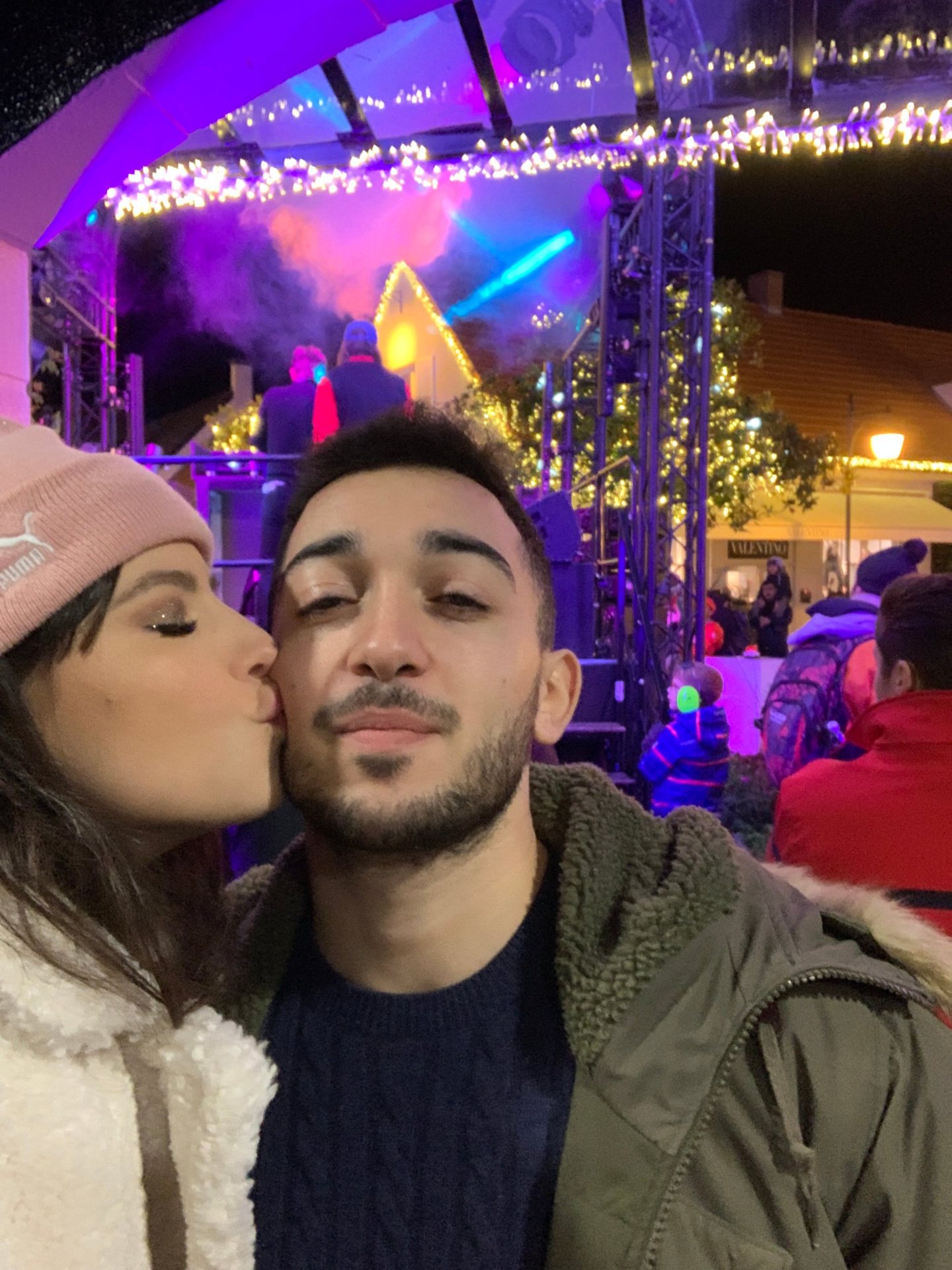 Betty Autier en bonnet rose fait un bisou à un ami pendant le DJ set des illuminations de Noël de La Vallée Village