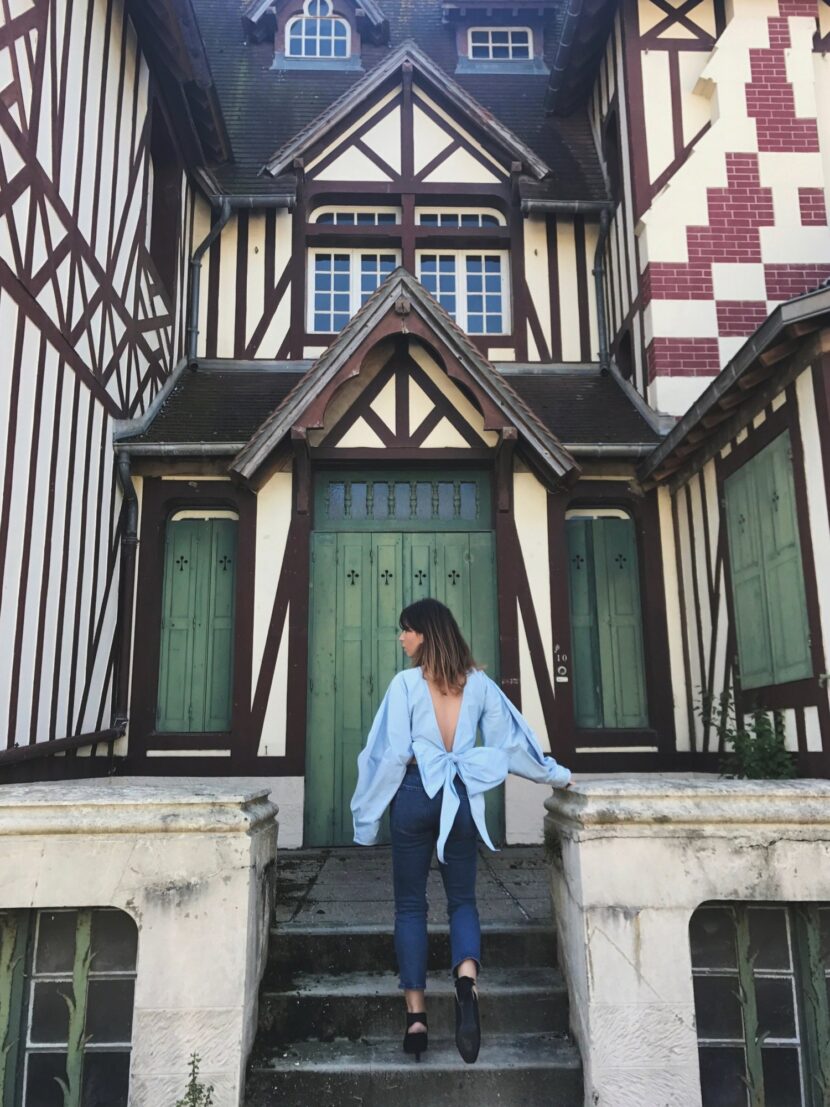 Betty Autier en top bleu dos nu noué devant une maison normande à Deauville