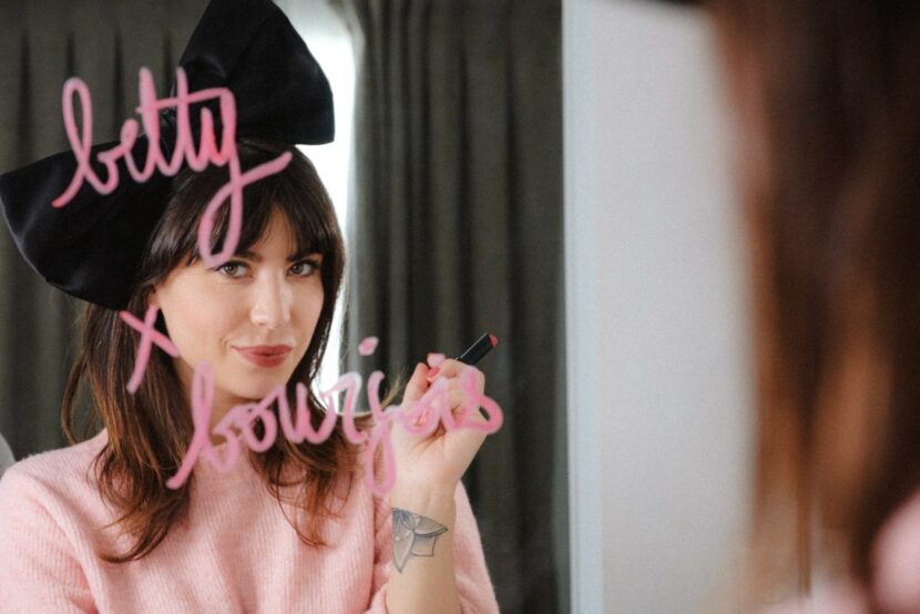 Betty Autier avec un nœud noir devant le miroir, lettrage Betty x Bourjois