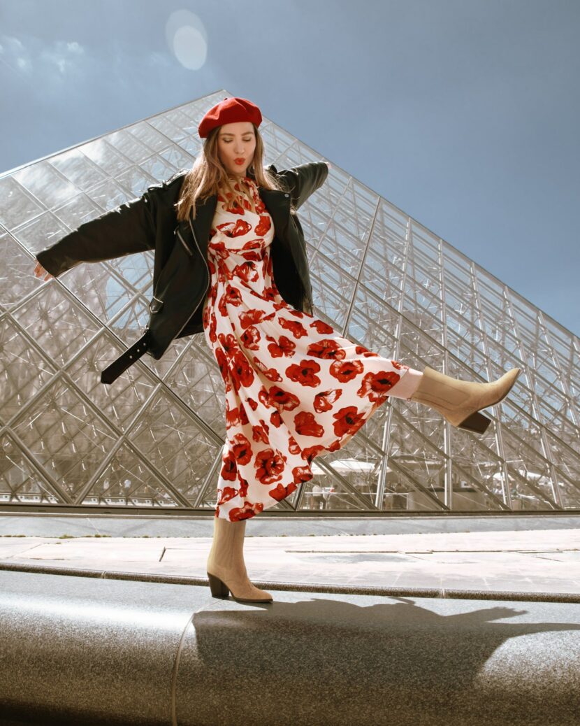 Betty Autier en robe coquelicots et bottines camel devant la Pyramide du Louvre