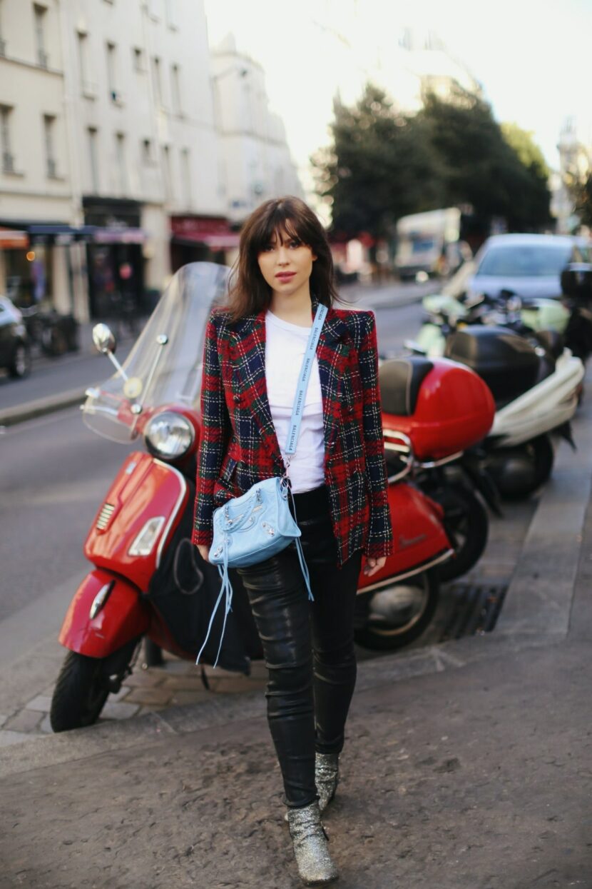 Betty Autier en blazer tartan avec un sac Balenciaga City bleu ciel devant un Vespa rouge