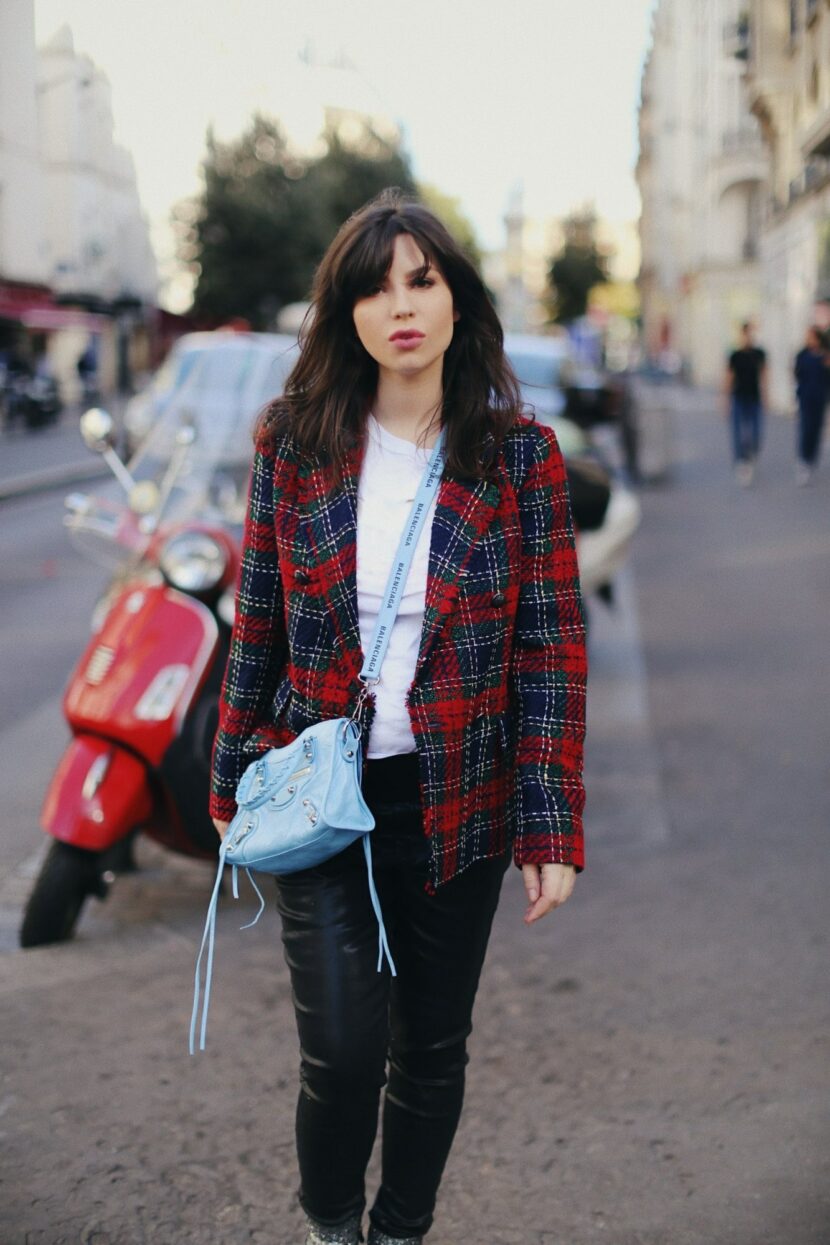 Betty Autier en blazer tartan rouge et pantalon en cuir à côté d'un Vespa rouge à Paris