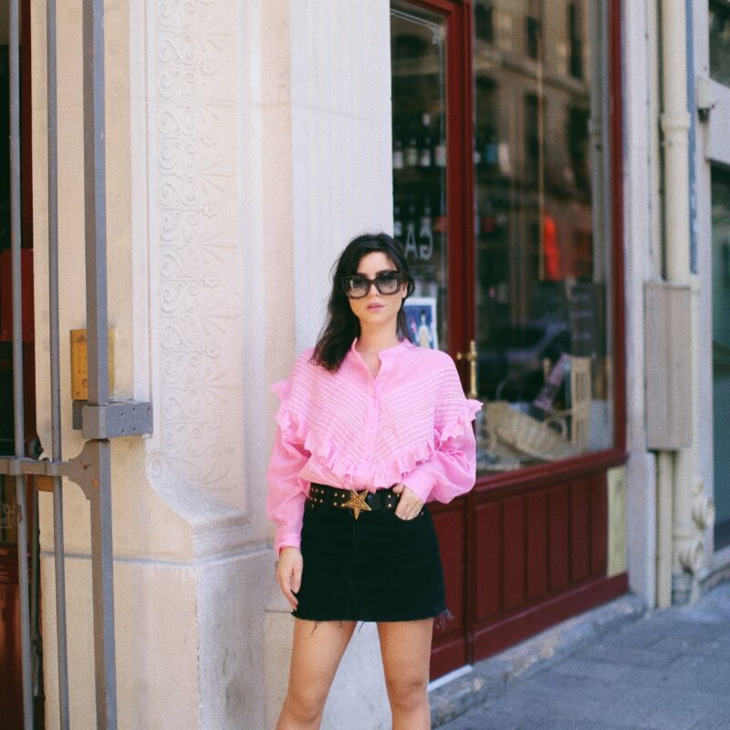 Betty Autier en blouse rose à volants, mini-jupe noire, ceinture étoile et mocassins blancs à Paris