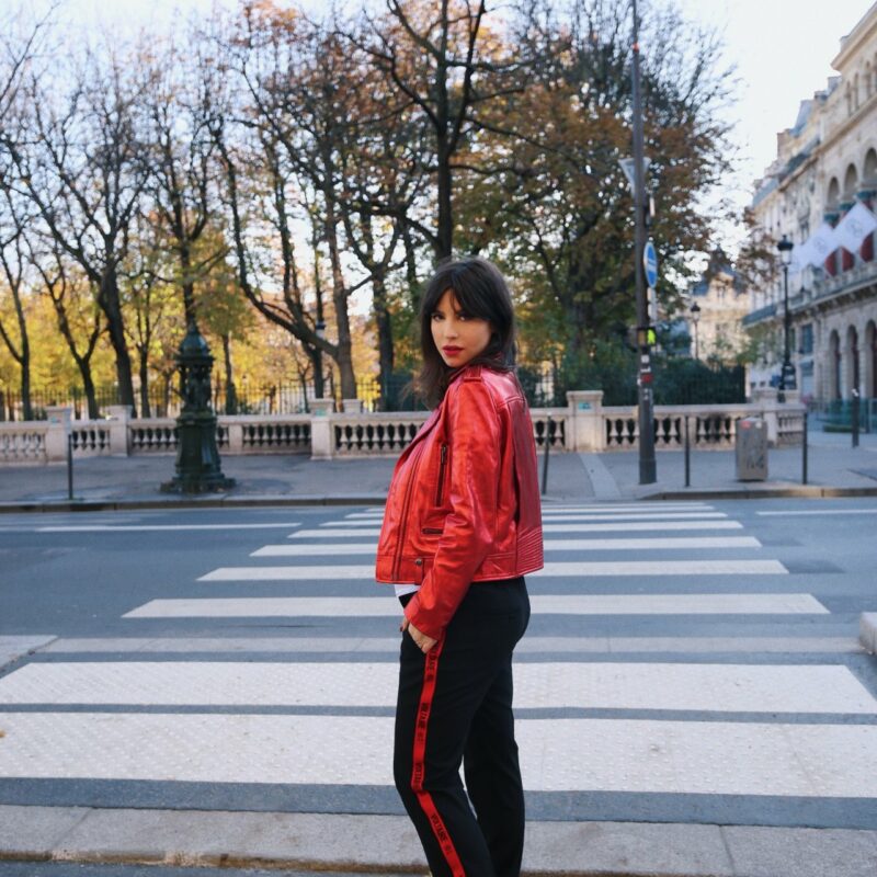 Betty Autier en perfecto rouge et pantalon noir à bande rouge Zadig & Voltaire sur un passage piéton à Paris