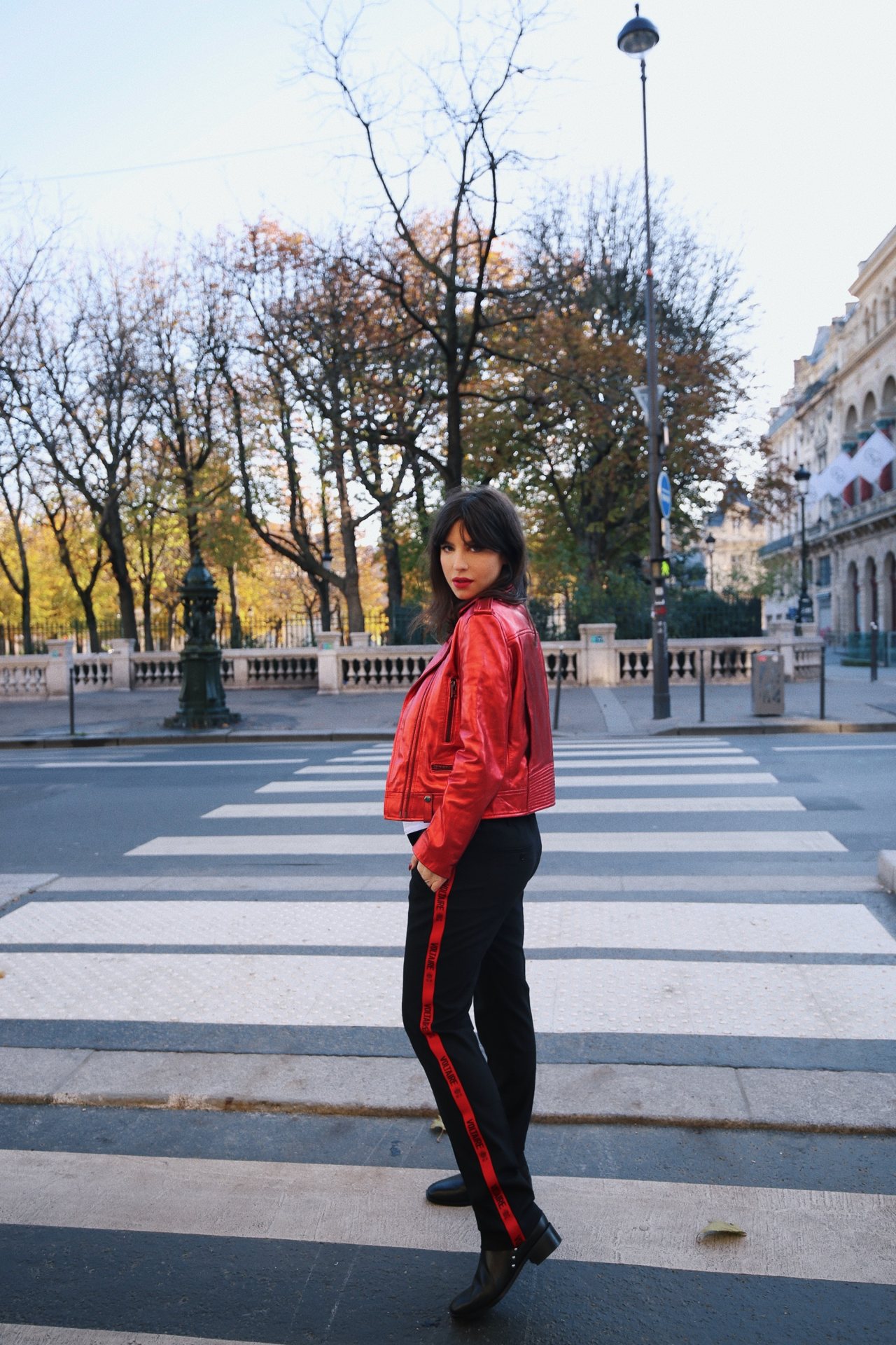 Betty Autier en perfecto rouge et pantalon noir à bande rouge Zadig & Voltaire sur un passage piéton à Paris