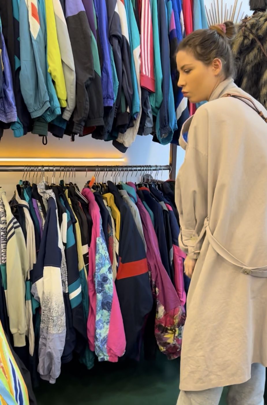 Betty chine devant un portant de vestes vintage colorées