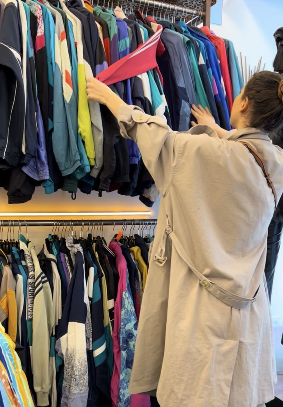 Portant de vestes de sport et coupe-vent vintage dans une friperie parisienne